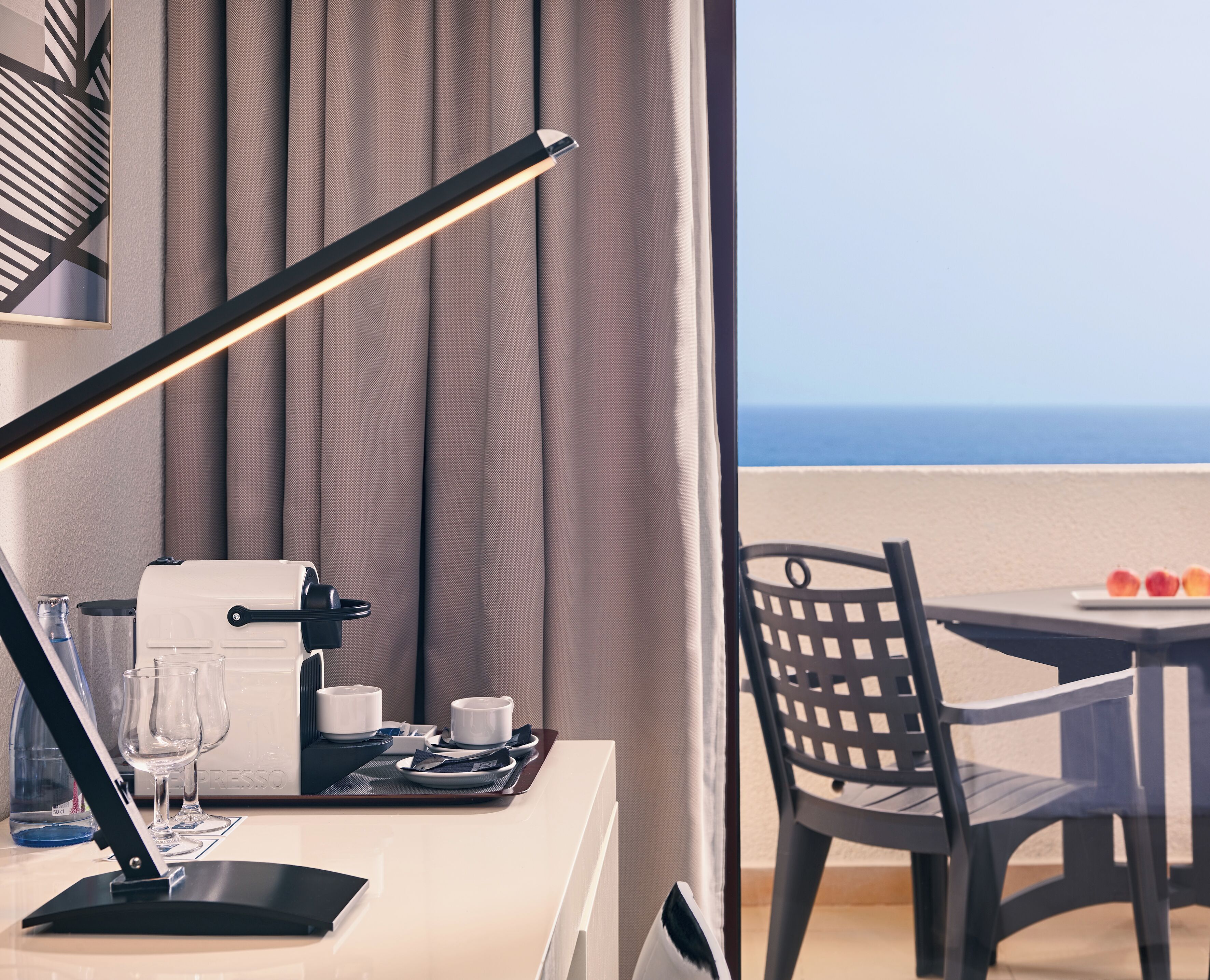 A hotel room with a desk, a coffee machine, and a view of the ocean.