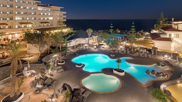 A resort with a large outdoor pool area, multiple lounge chairs, and a view of the ocean. - H10 Taburiente Playa (Brena Baja)