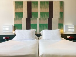 Habitación de hotel con dos camas, un cuadro abstracto grande en la pared y lámparas fijadas a la pared.