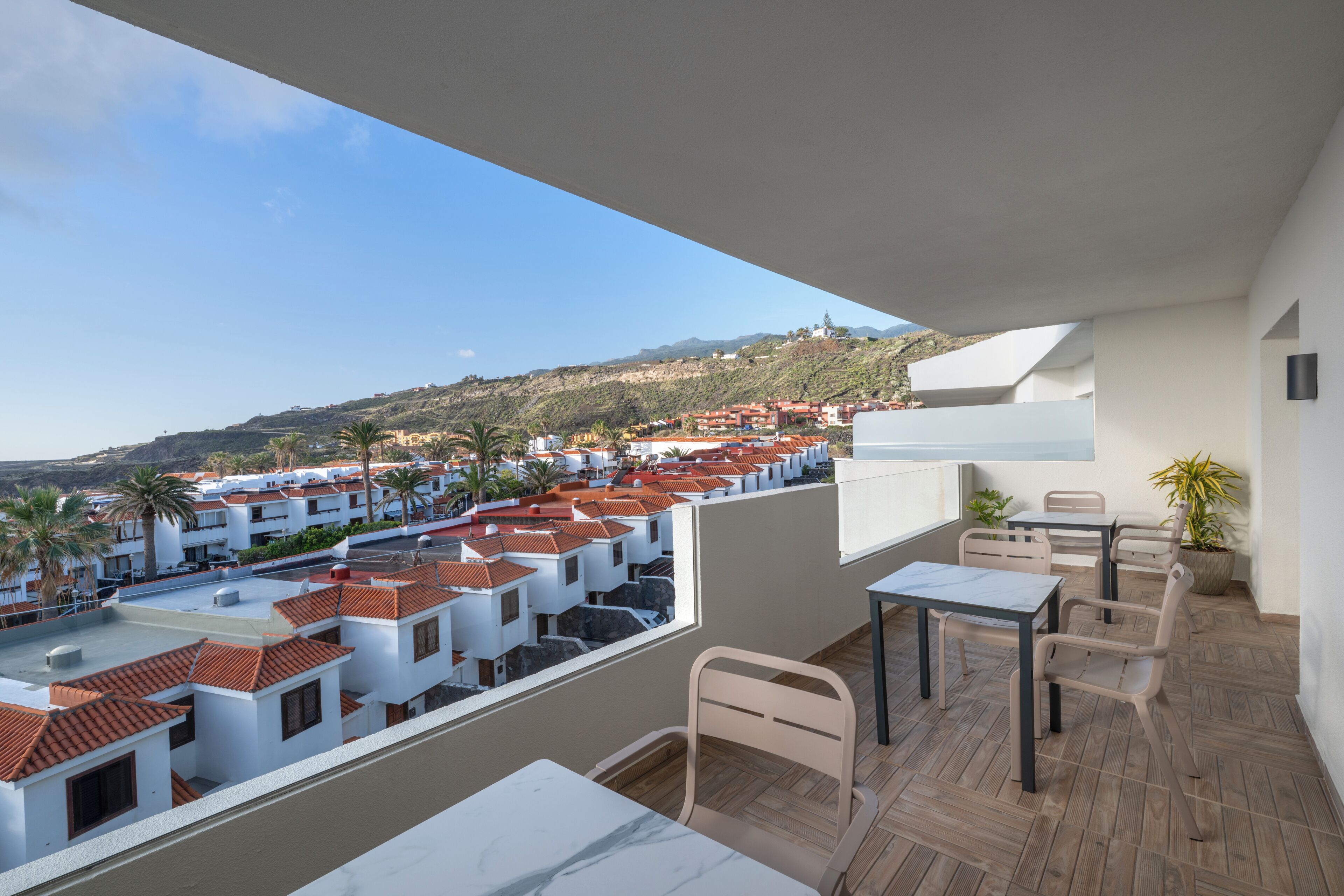 A balcony with a view of a residential area, a table, and chairs.