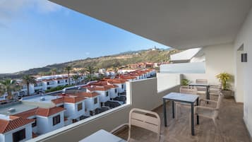 A balcony with a view of a residential area, a table, and chairs.