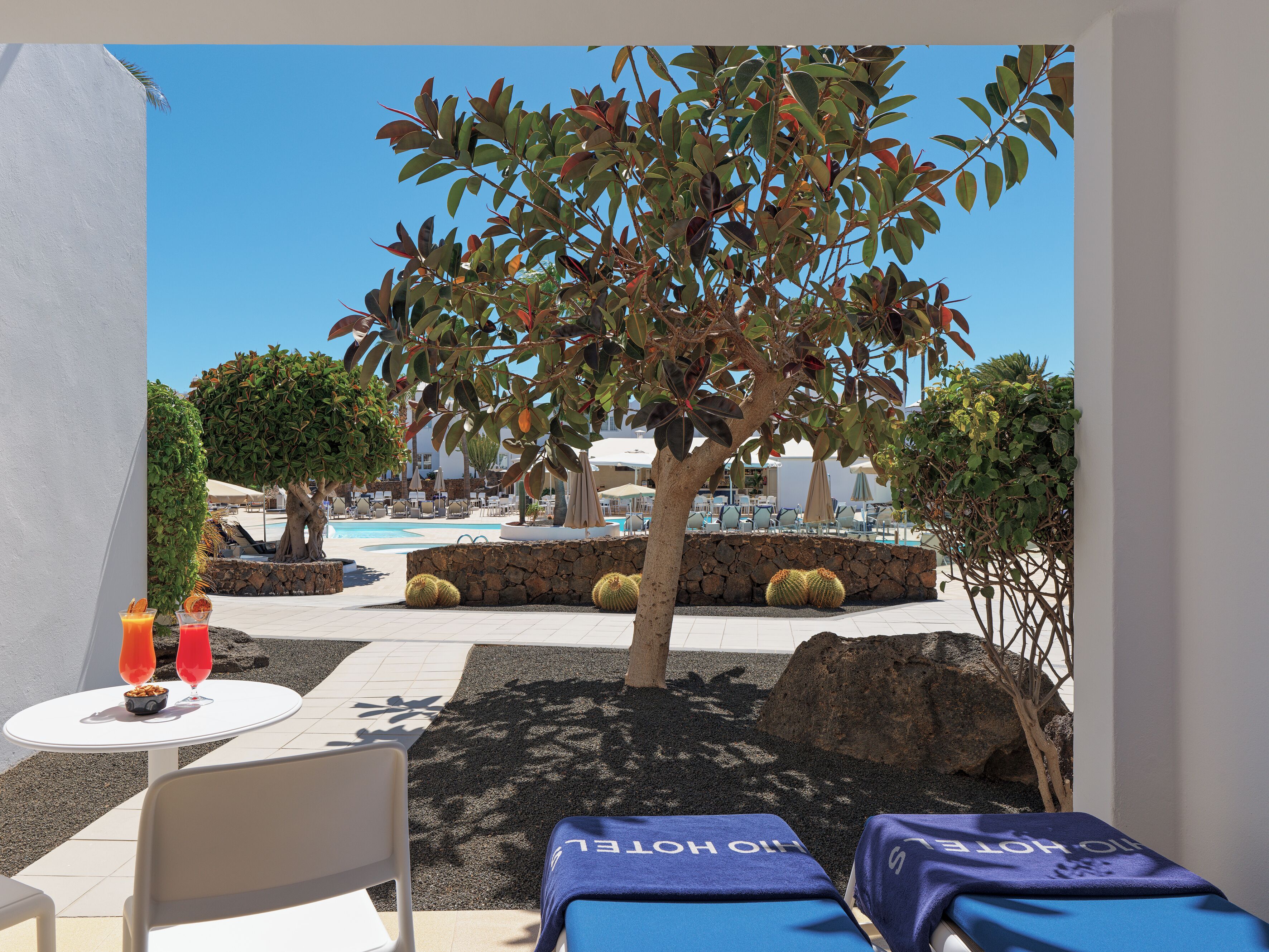 A poolside area with lounge chairs, a table with drinks, and a view of the pool and resort buildings.
