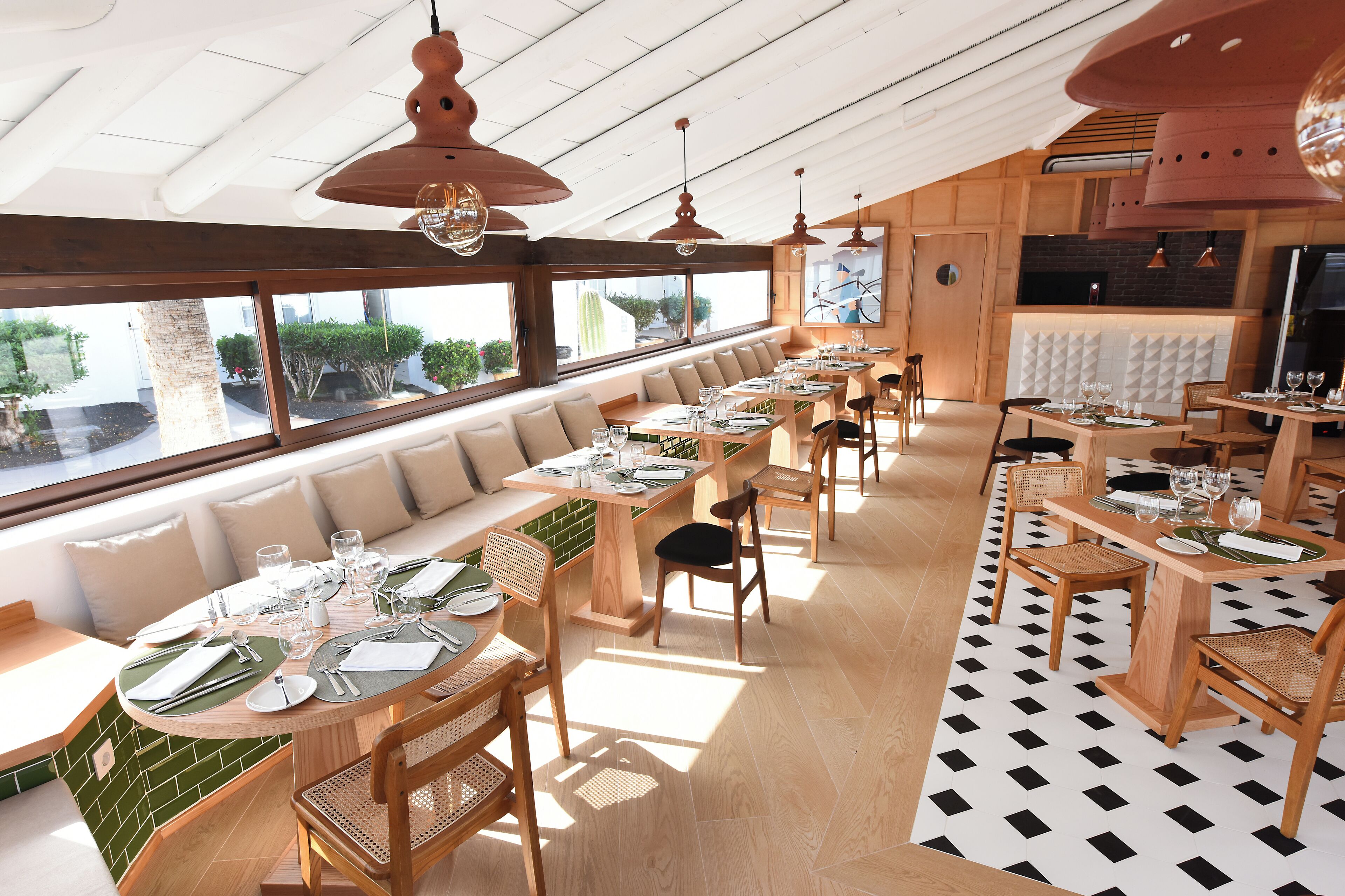 A restaurant with long communal tables, wooden chairs, and a view of the outdoors.
