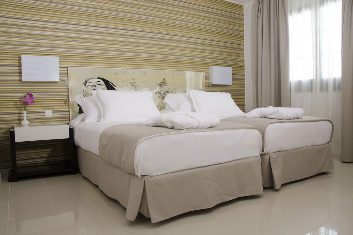 A hotel room with a large bed, a bedside table with a vase of flowers, and a wall-mounted air conditioning unit.