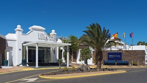A boutique hotel entrance with a covered patio, palm trees, and a clear blue sky. - H10 White Suites (Yaiza)