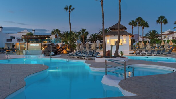 Una piscina con sillones de descanso y palmeras.