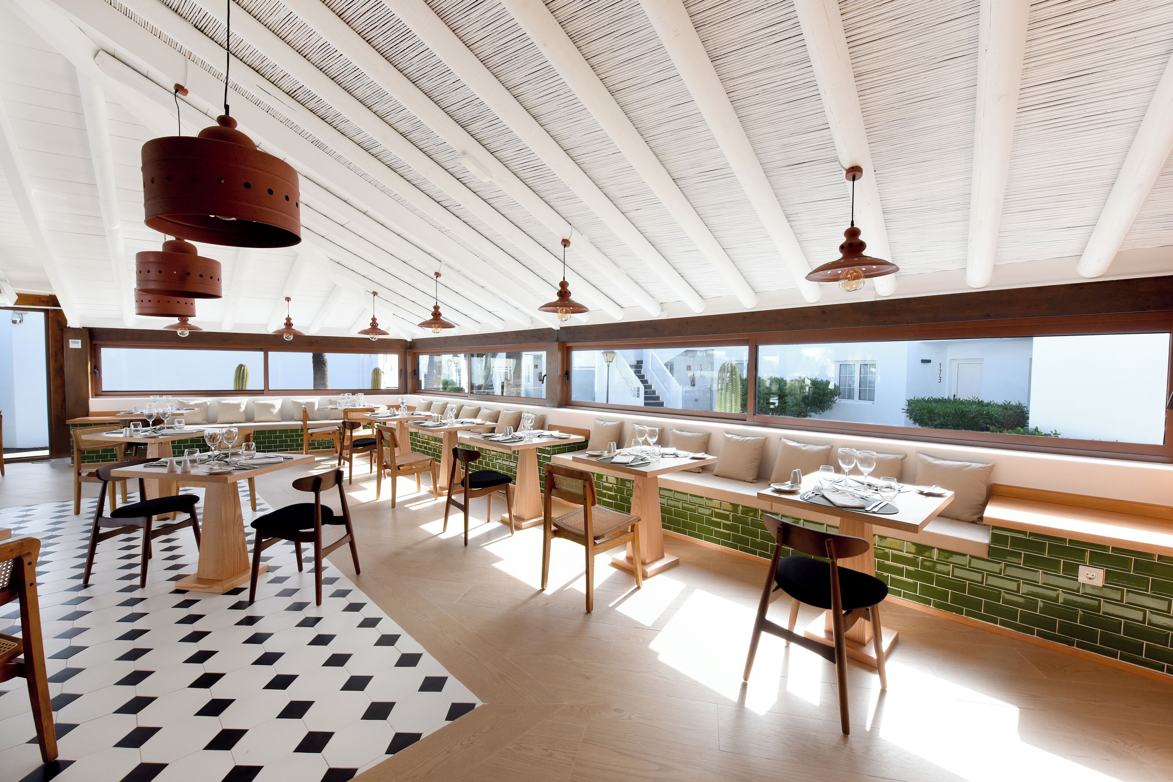 Een modern restaurant met lange gedeelde tafels, comfortabele zitplaatsen en grote ramen met uitzicht op de omgeving.