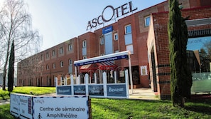 Un bâtiment sur lequel on peut lire l’inscription « ASCOTEL » et qui possède un espace extérieur couvert portant la mention « Centre de séminaire Amphithéâtre ».