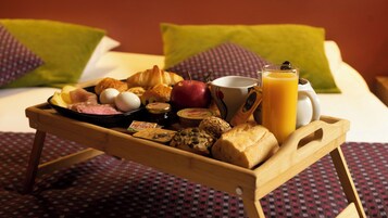 Bandeja de desayuno con huevos, jamón, pan, una manzana y jugo, sobre una cama con almohadas y una colcha estampada.
