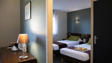 A hotel room with two beds, a desk with a lamp, a bedside table with a phone, and a wall-mounted light.