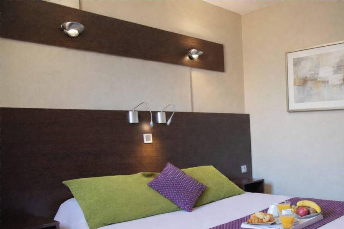 Ein Hotelzimmer mit Bett, Kopfteil, Wandleuchte, einem gerahmten Bild und Tablett auf dem Bett.