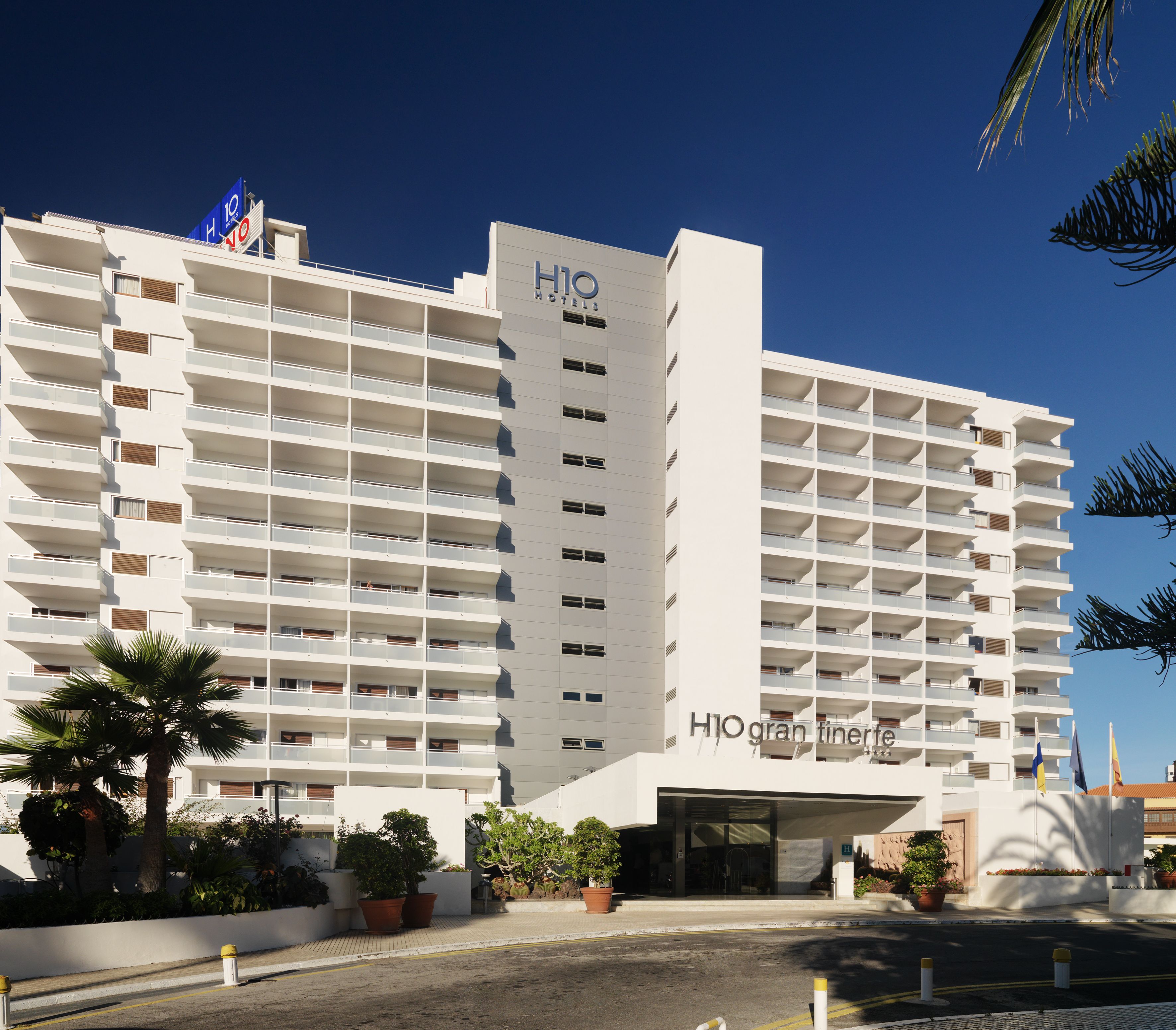 Un hotel de varios pisos con diseño moderno, que cuenta con balcones en cada planta y una entrada destacada.