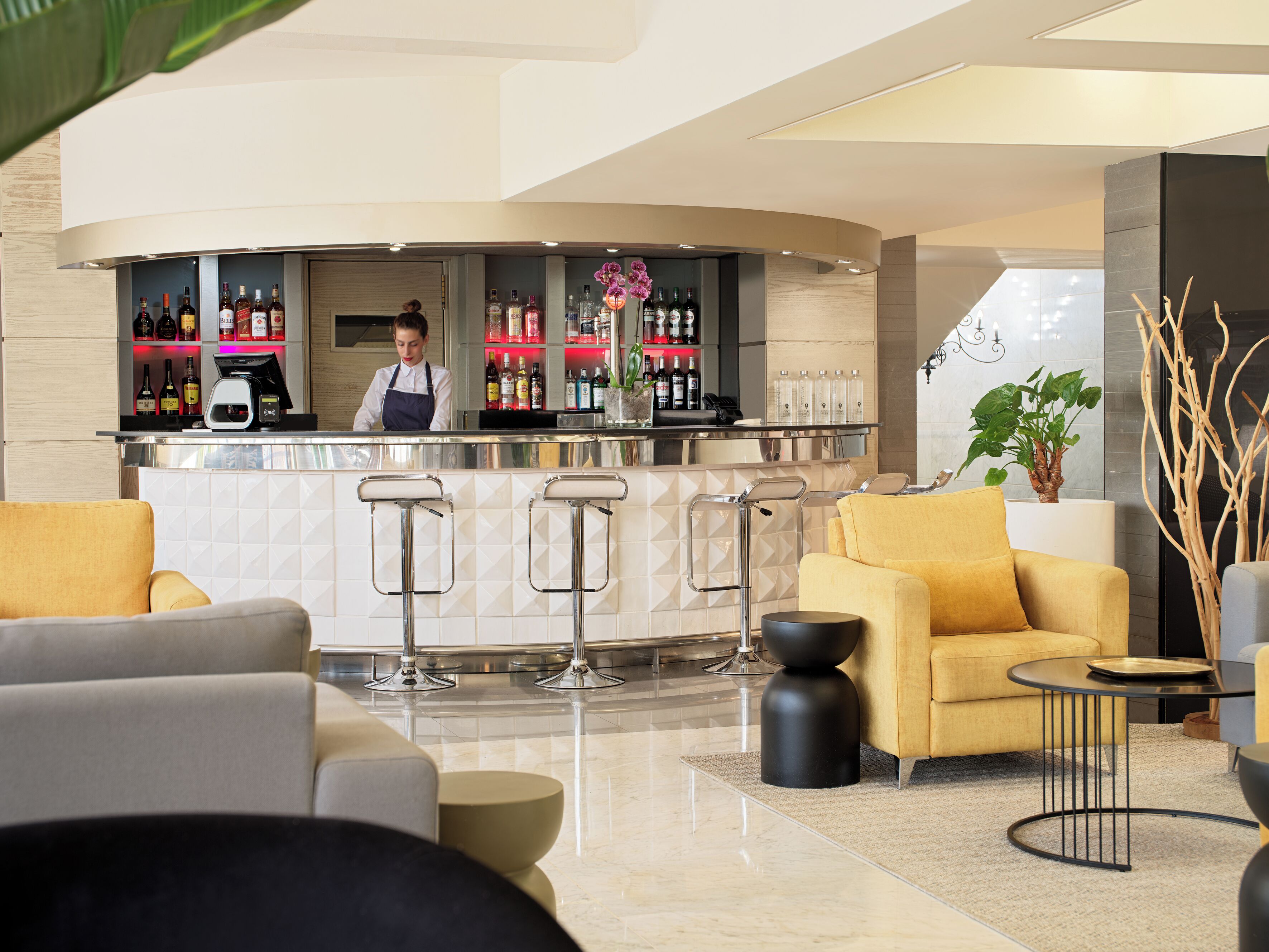 Un área de bar moderna con un barman, taburetes y una variedad de botellas de licor.