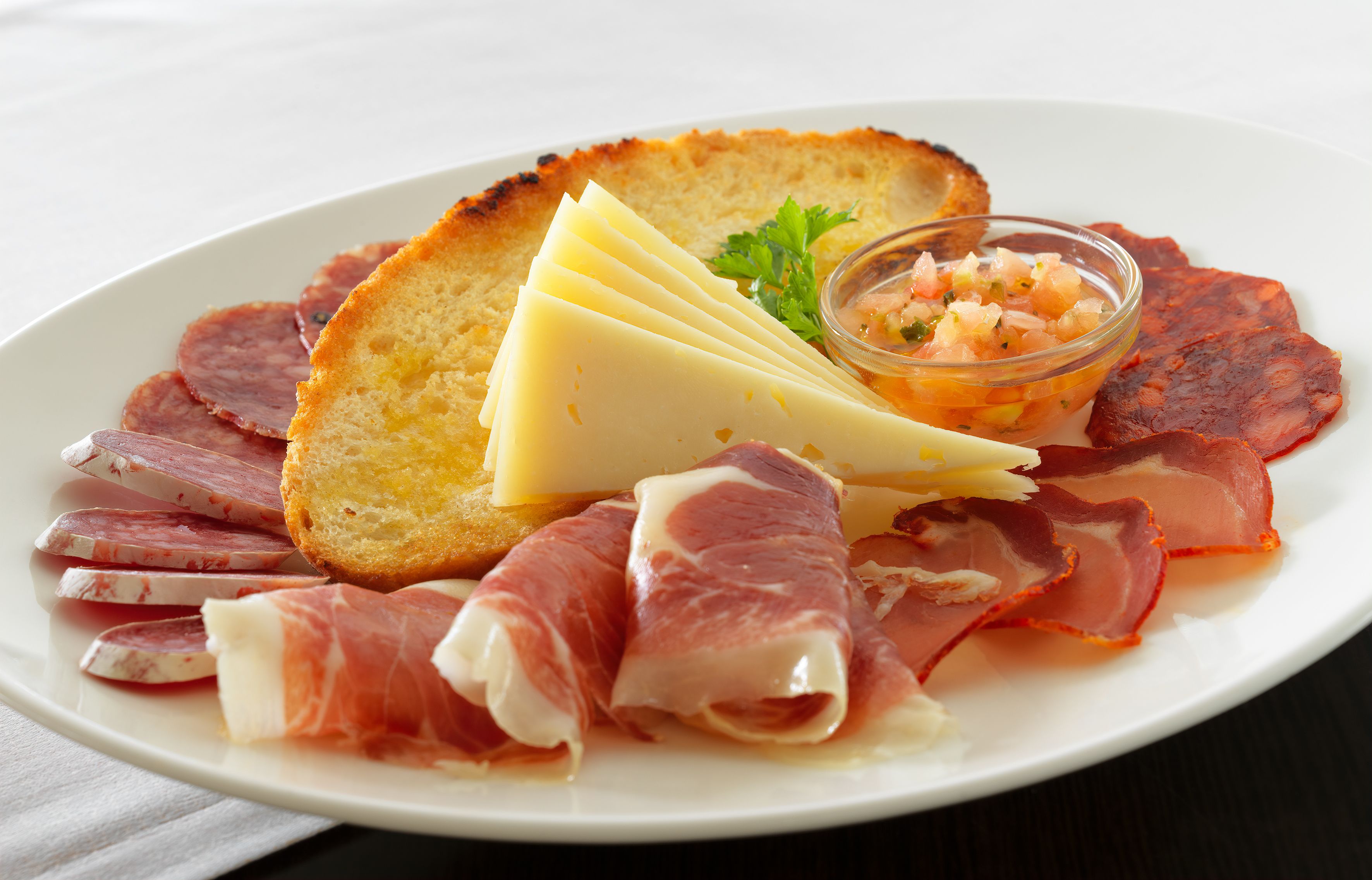Une assiette de nourriture comprenant différentes sortes de viandes, du fromage et un petit bol de salsa.
