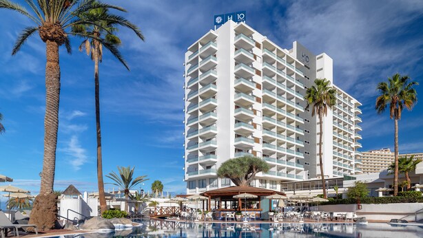 Un hotel con piscina, palmeras y un cielo azul despejado.