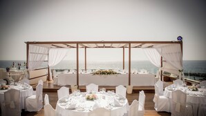 Montaje para una boda al aire libre con mesas redondas y sillas blancas, con vista al mar.