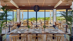 A restaurant with a view of the ocean, featuring wooden tables and chairs, and large windows.