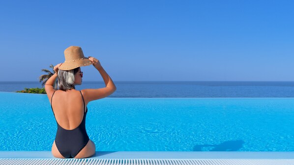 A person sitting by a pool with a clear view of the ocean.