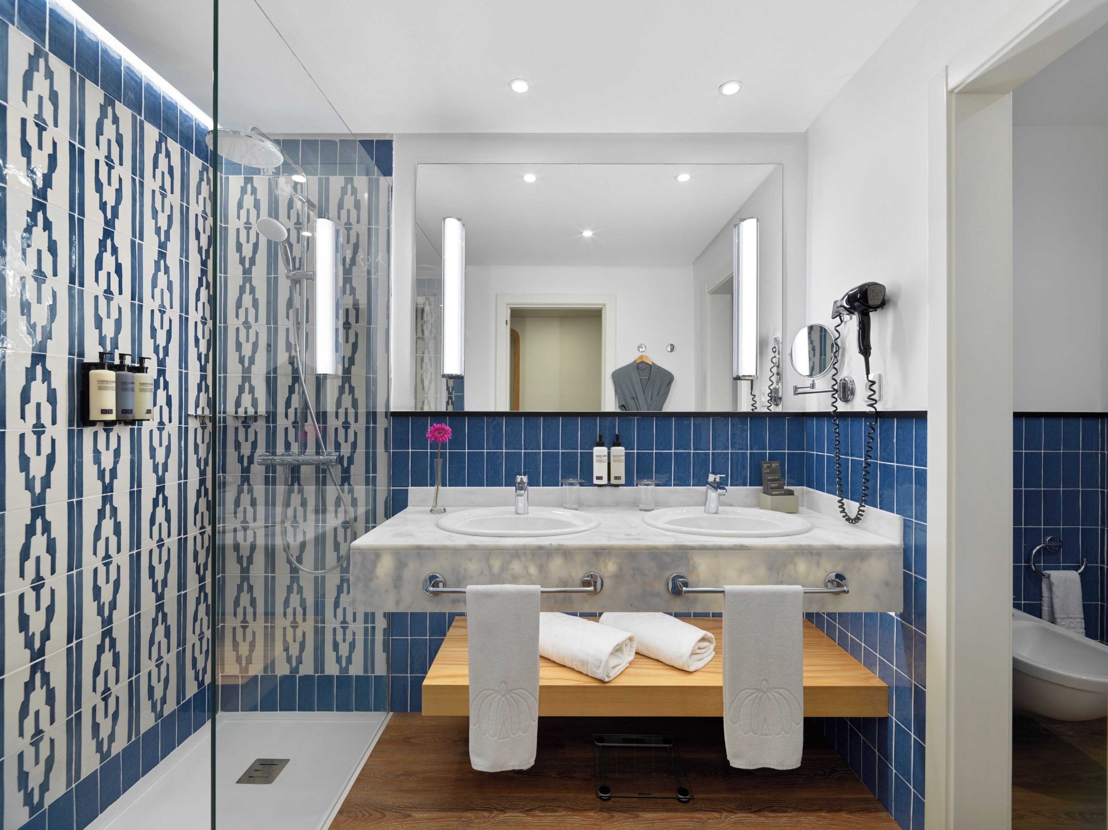 A modern bathroom with a glass shower enclosure, two sinks, and a wooden vanity.
