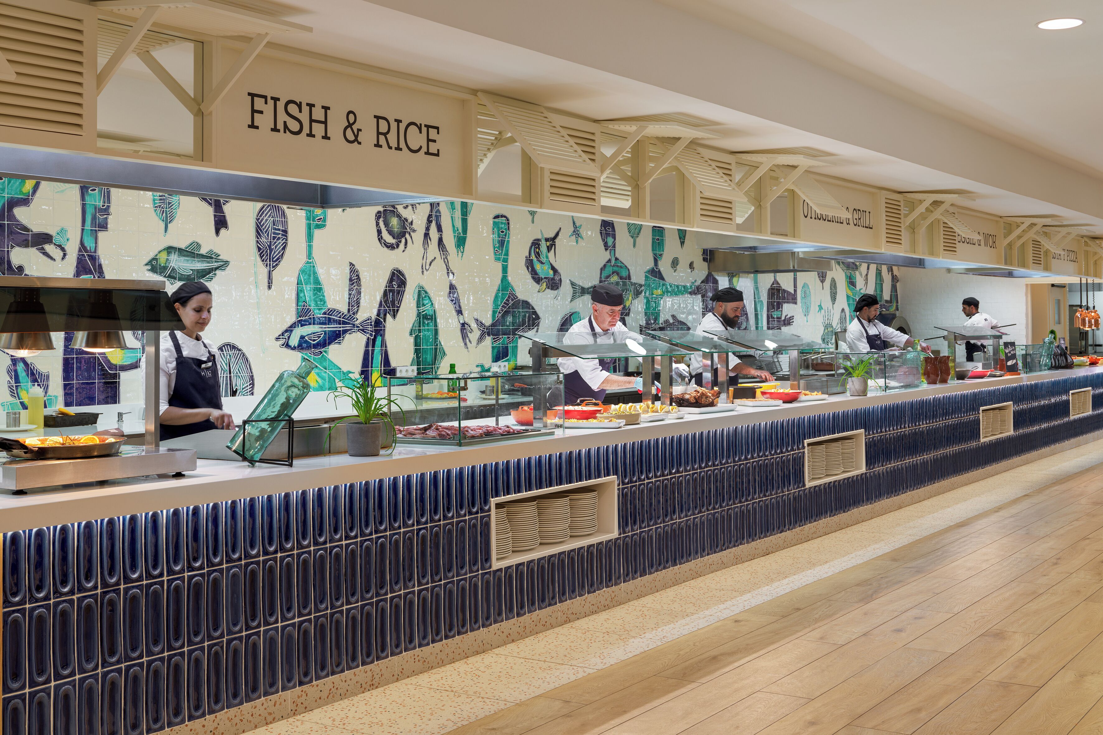 Un espace buffet agrémenté d’une enseigne indiquant « POISSON ET RIZ », de plusieurs points de service et d’un mur recouvert de carreaux décorés de motifs de poissons.