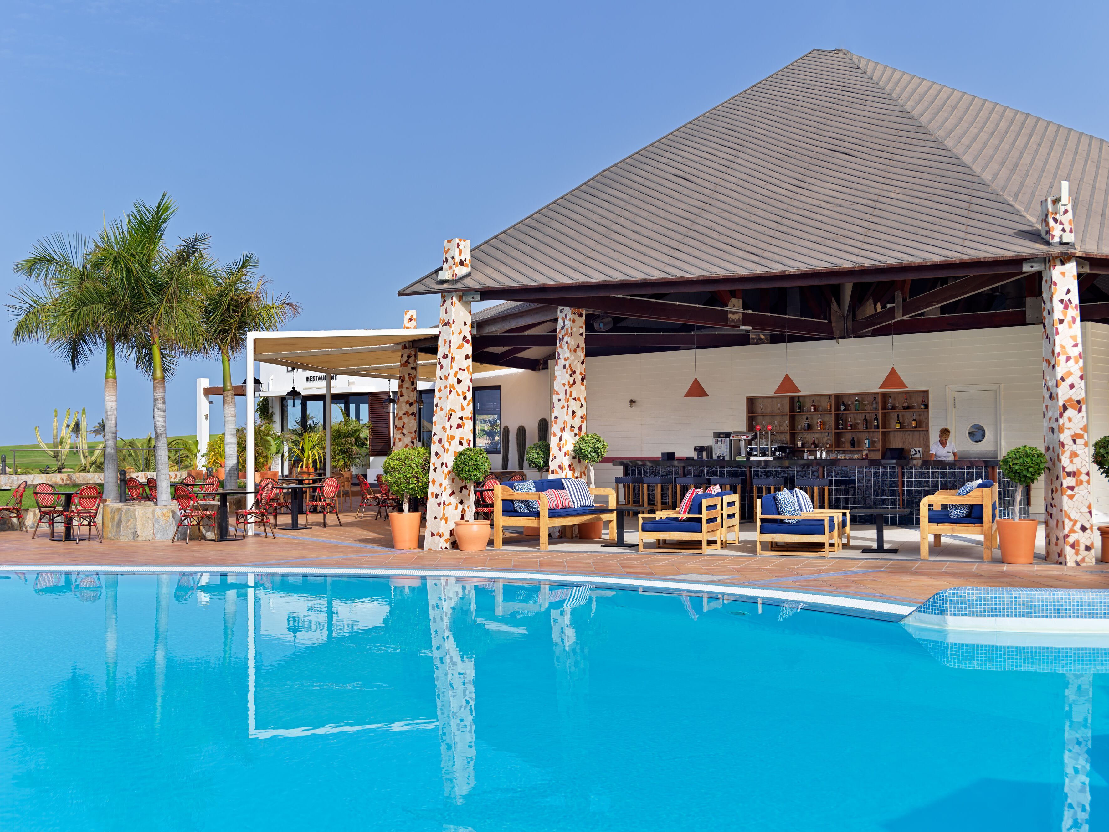 A poolside area with lounge chairs, a bar, and a restaurant.