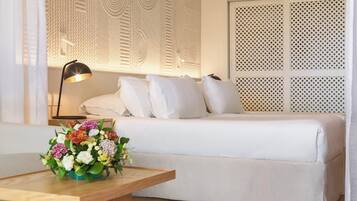 A neatly arranged hotel room with a bed, a bedside table with a lamp, and a floral arrangement.