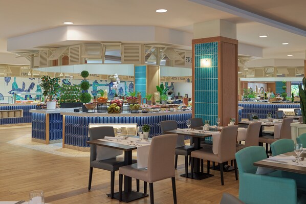 Um restaurante moderno com área de bar central, diversas opções de assento, e variedade de plantas e frutas expostas.