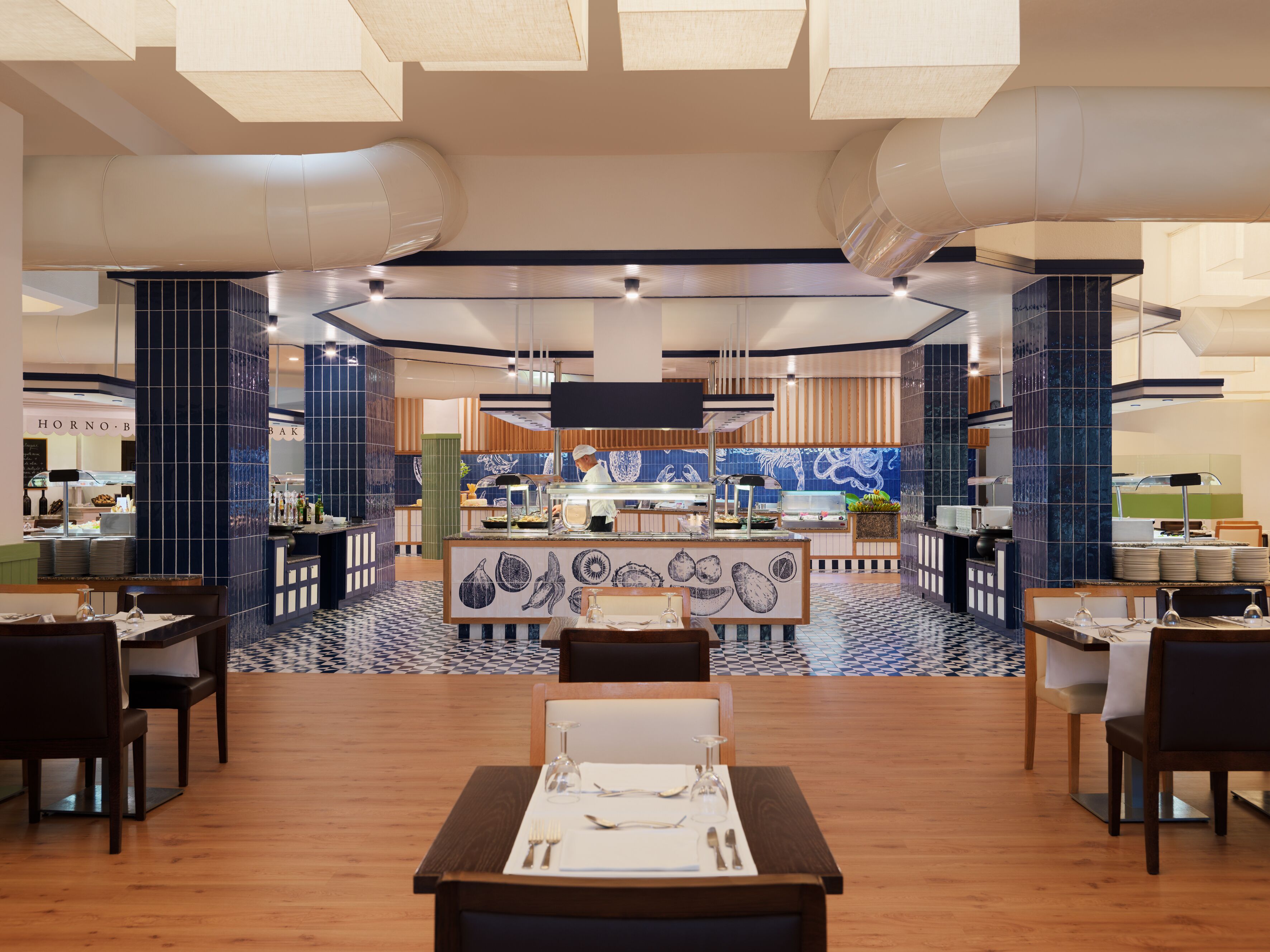 A modern restaurant with a central counter, dining tables, and a patterned floor.