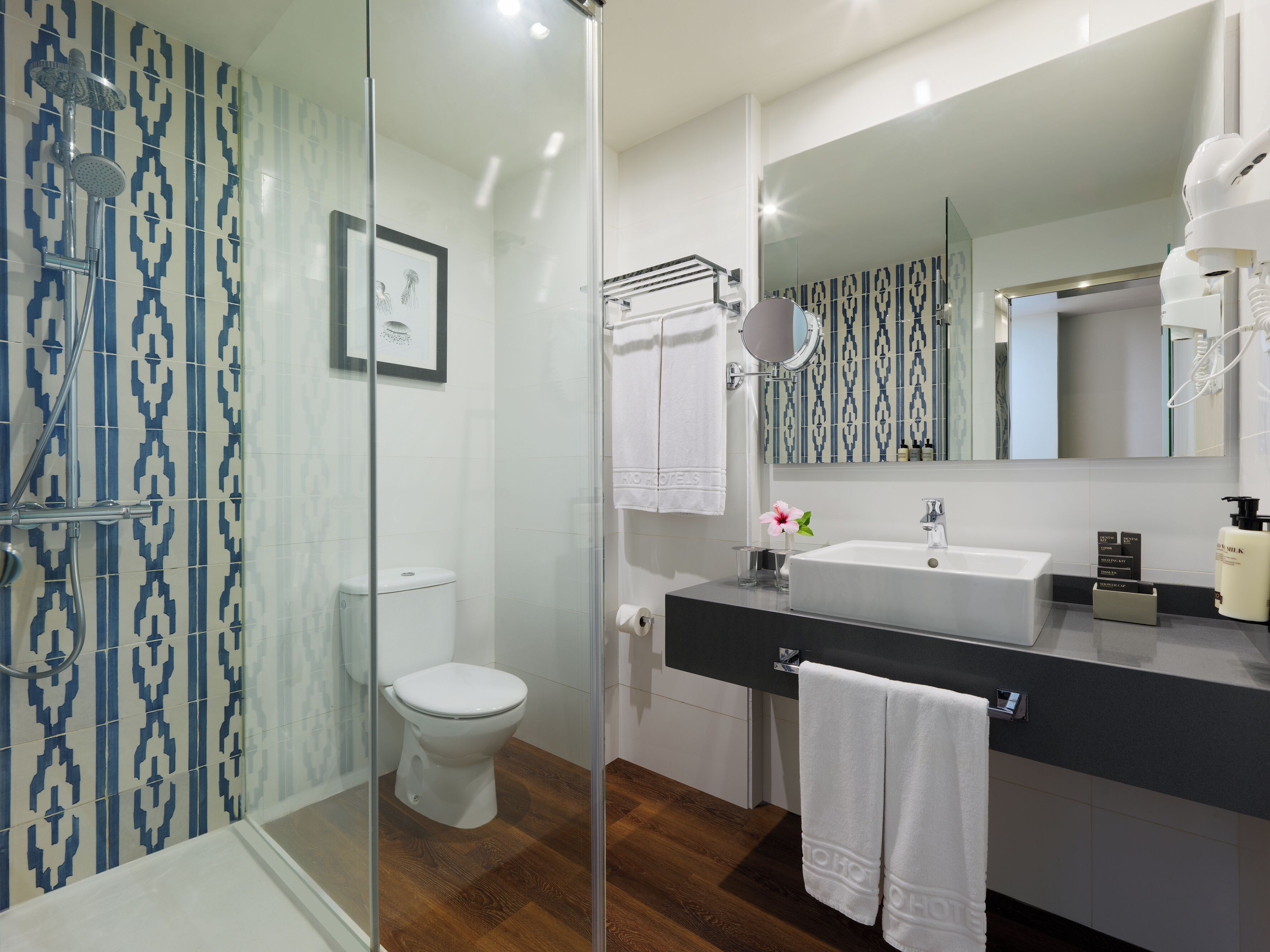 A modern bathroom with a glass shower enclosure, a toilet, a sink with a mirror, and a wooden floor.