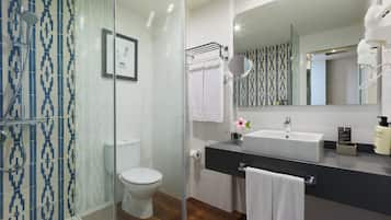 A modern bathroom with a glass shower enclosure, a toilet, a sink with a mirror, and a wooden floor.