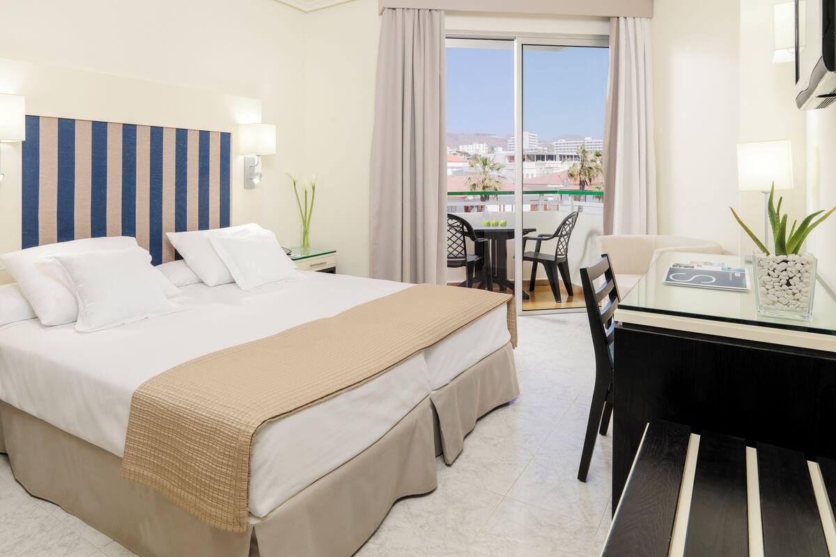 A hotel room with a bed, a desk, and a balcony with a view of buildings.