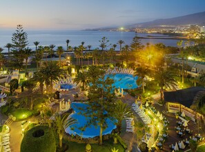 A resort with multiple swimming pools, palm trees, and a view of the sea. - H10 Las Palmeras (Arona)
