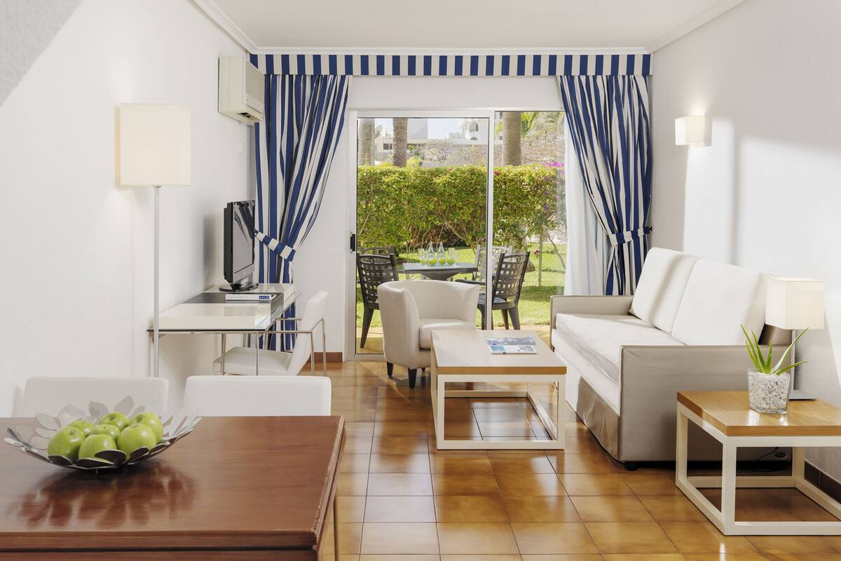 Una sala de estar moderna con televisión, sofá, mesa de centro y zona de comedor.