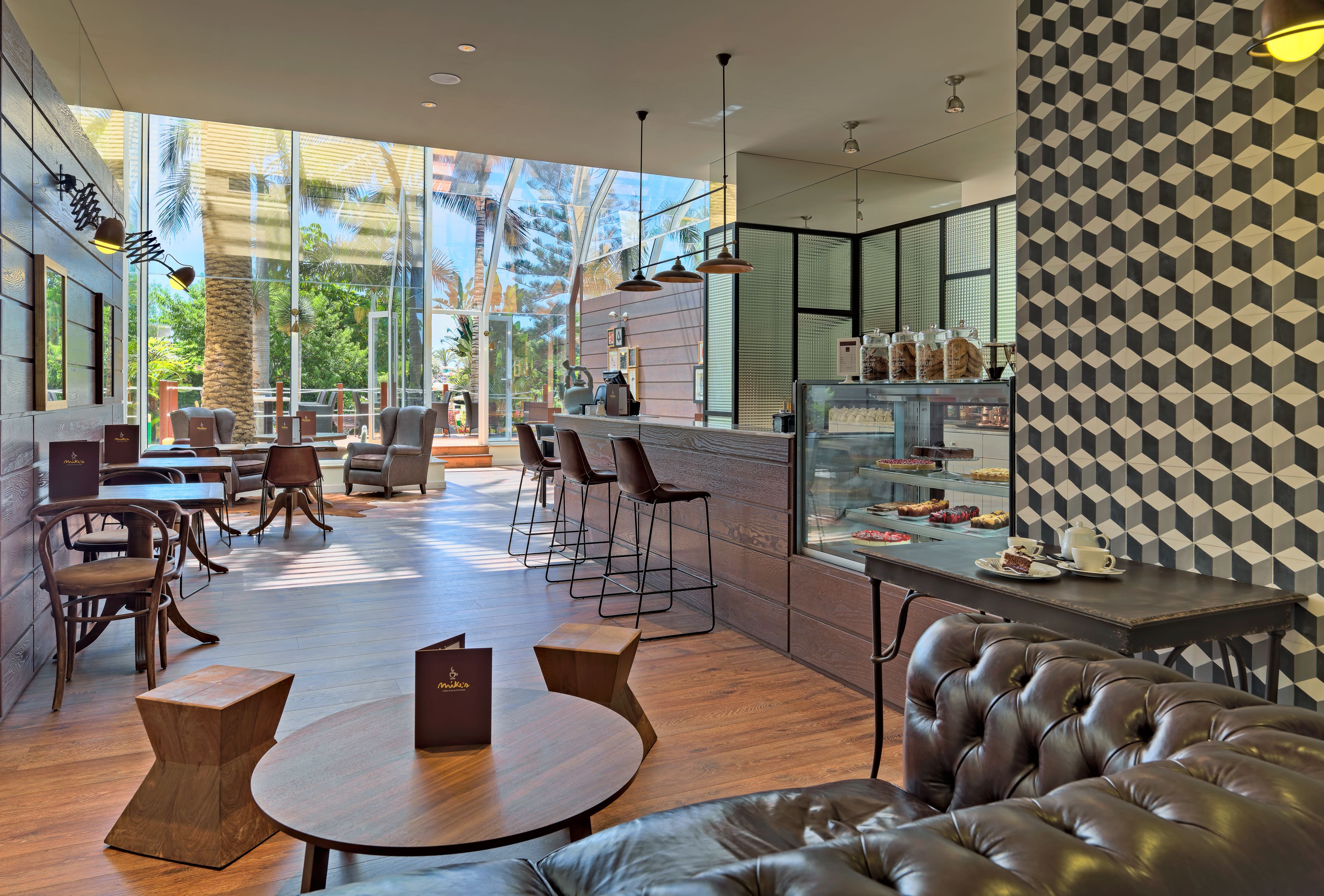 Un café moderno con suelo de madera, asientos de cuero y una vitrina de vidrio con pasteles.