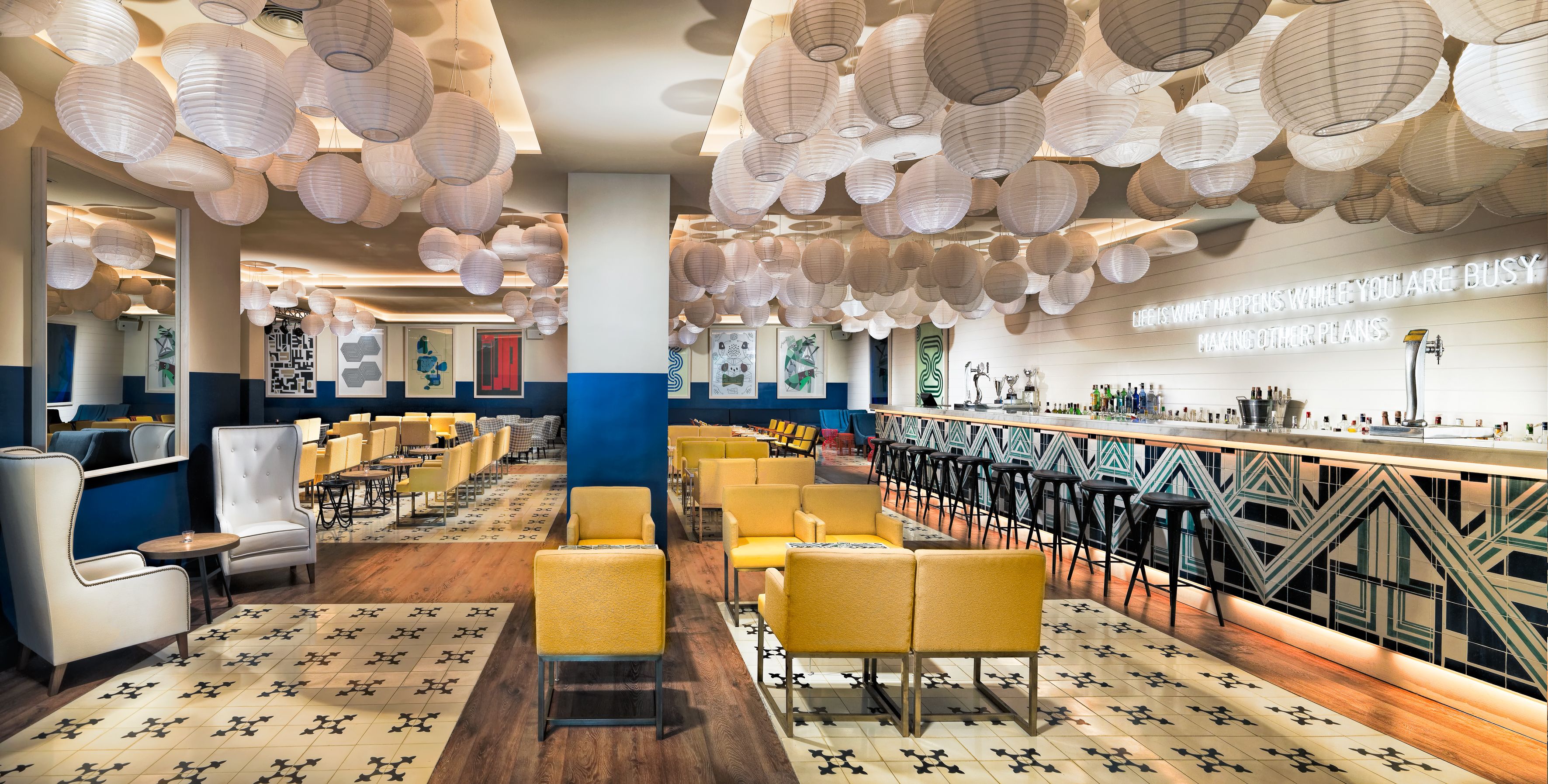 Un restaurante con sillas amarillas, una zona de bar y farolillos de papel colgantes.