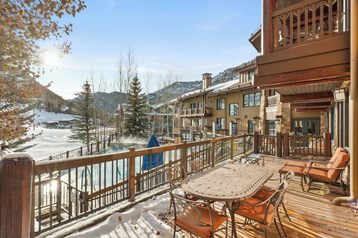 A wooden deck with outdoor seating, overlooking a snowy landscape and a river.