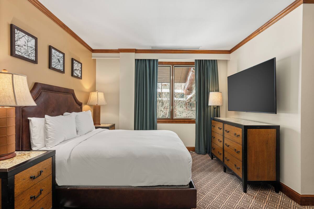 A hotel room with a bed, a dresser, a TV, and a window with curtains.