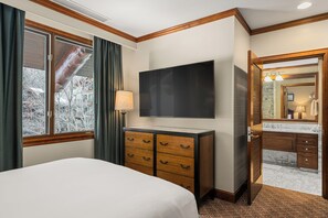 A hotel room with a bed, a TV, a dresser, a window with curtains, and a bathroom with a mirror and sink. - Ritz-Carlton Club, Aspen Highlands by Frias (Aspen)