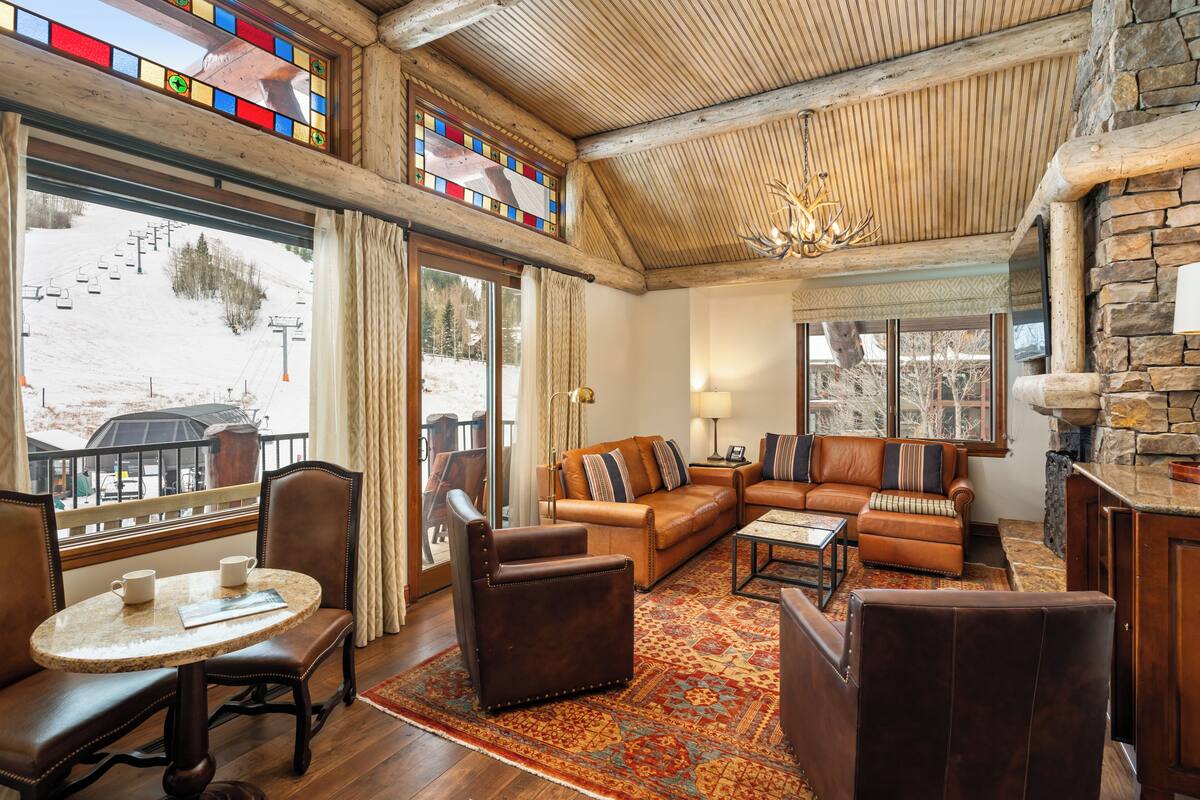 A cozy living room with a fireplace, leather furniture, and large windows overlooking a snowy landscape.