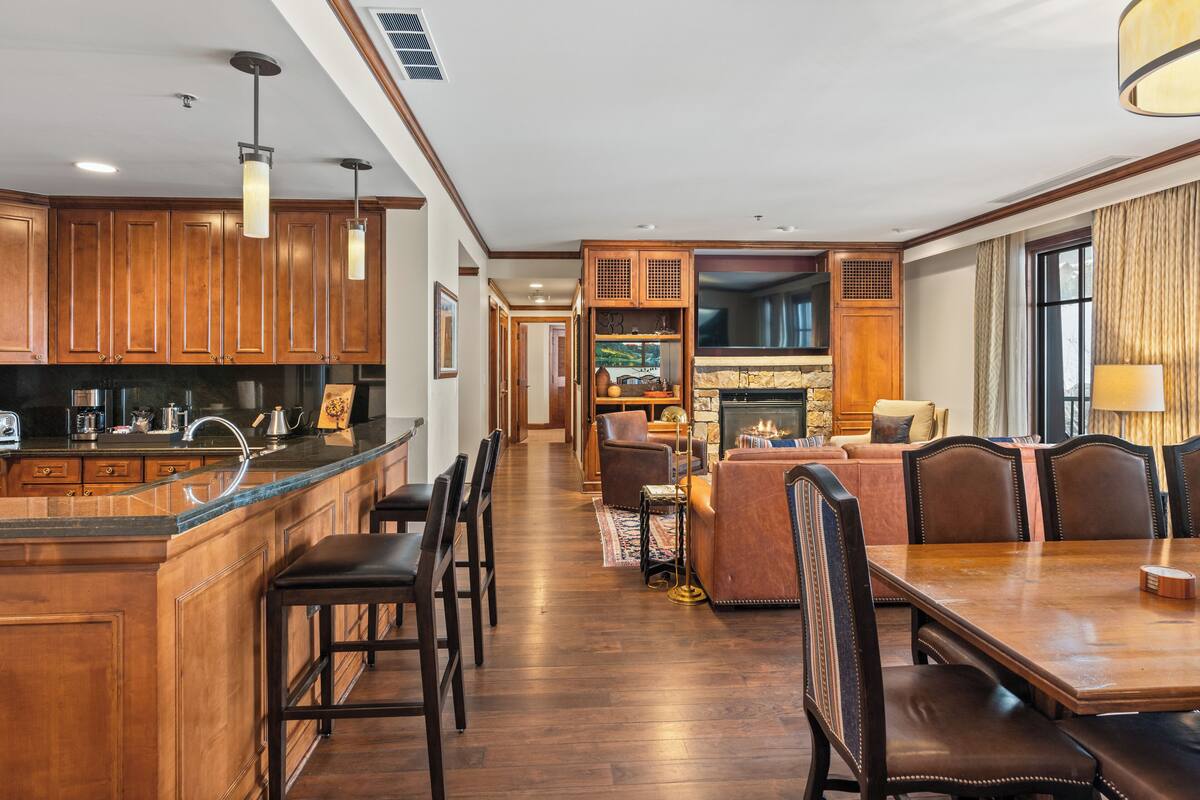 A spacious kitchen with wooden cabinets, a central island, and bar stools. There is a dining area with a wooden table and chairs.