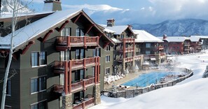 Een hotel met meerdere verdiepingen, balkons en een verwarmd buitenzwembad, omringd door sneeuw.