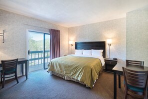 A hotel room with a bed, two bedside tables, a desk, two chairs, and a large window with a view of greenery.