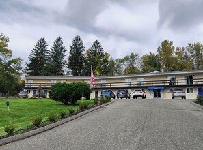 Um motel com entrada central, uma bandeira e área de estacionamento com vários carros.