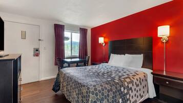 Habitación de hotel con una cama grande, dos lámparas de noche, un escritorio con silla, una ventana con cortinas y una puerta con placa.