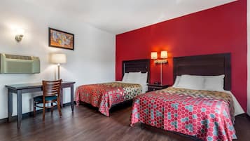 A hotel room with two beds, a desk, a chair, and a wall-mounted air conditioner.