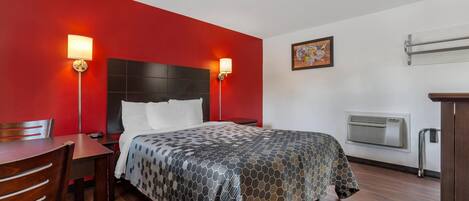 Habitación de hotel con cama, escritorio, silla, aire acondicionado de pared y dos lámparas de pared.