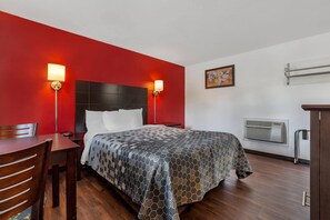 A hotel room with a bed, a desk, a chair, a wall-mounted air conditioner, and two wall-mounted lamps. - Econo Lodge Lee - Great Barrington (Lee)