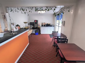 A compact kitchen with a counter, a microwave, a coffee machine, and a refrigerator. There is a dining area with a table and chairs. - Econo Lodge Lee - Great Barrington (Lee)