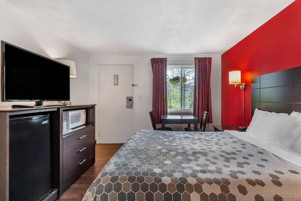 A hotel room with a bed, a television, a desk, and a window with curtains.
