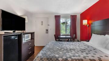A hotel room with a bed, a television, a desk, and a window with curtains.